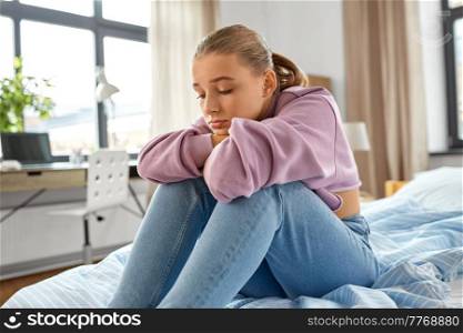 sadness, mental health and people concept - sad girl sitting on bed at home. sad girl sitting on bed at home