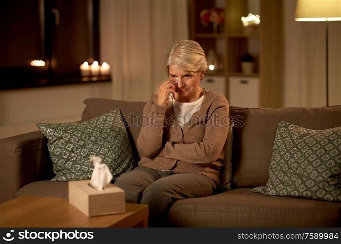 sadness, stress and people concept - unhappy crying senior woman wiping tears with paper tissue at home at night. crying senior woman wiping tears with paper tissue