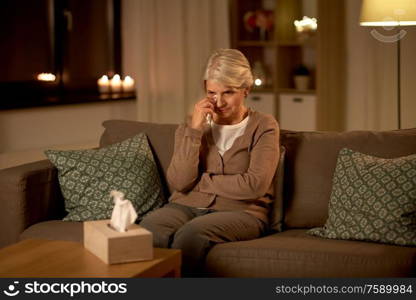 sadness, stress and people concept - unhappy crying senior woman wiping tears with paper tissue at home at night. crying senior woman wiping tears with paper tissue