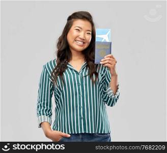 safe travel, tourism and health care concept - happy smiling young asian woman with air ticket and immunity passport over grey background. asian woman with air ticket and immunity passport