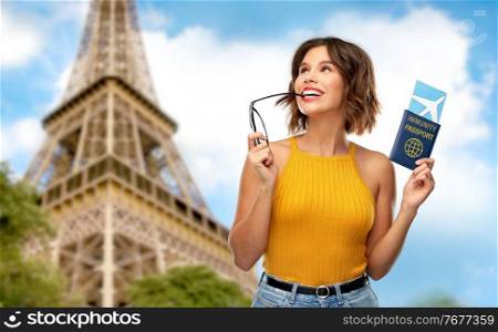 safe travel, tourism and health care concept - happy smiling young woman with air ticket and immunity passport over eiffel tower in paris background. happy woman with air ticket and immunity passport