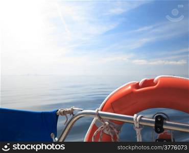 Safe water support aid circle. Rescue red lifebuoy life preserver saver ring on sailboat and blue sky baltic sea.