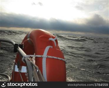 Safe water support aid circle. Rescue red lifebuoy life preserver saver ring on sailboat and stormy clouds overcast sky baltic sea.