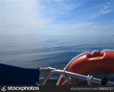 Safe water support aid circle. Rescue red lifebuoy life preserver saver ring on sailboat blue sky baltic sea. The Oresund bridge between Denmark and Sweden in the background.