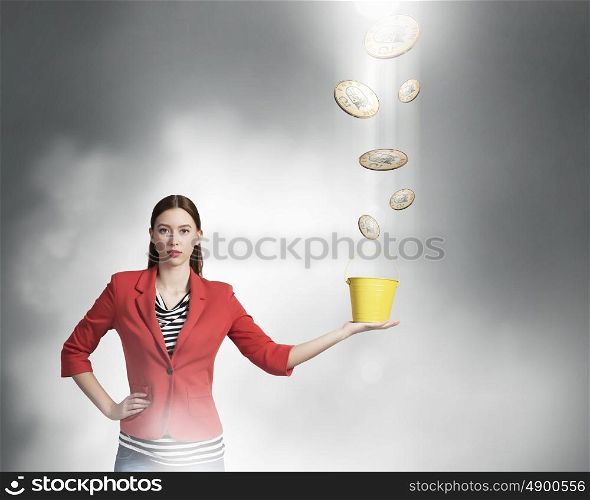 Safekeep your money. Young woman holding yellow bucket with euro coins flying out