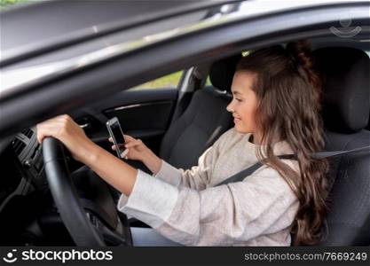 safety and people concept - happy smiling young woman or female driver with smartphone driving car in city. smiling woman or female driver driving car in city