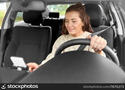 safety and people concept - happy smiling young woman or female driver with smartphone driving car in city. smiling woman or female driver driving car in city
