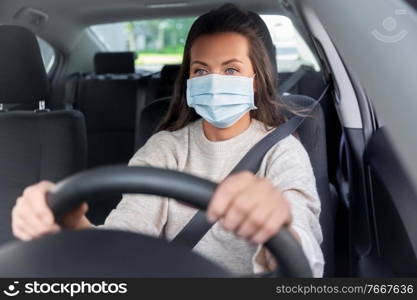 safety and people concept - young woman or female driver in medical mask driving car in city. woman or female driver in mask driving car in city