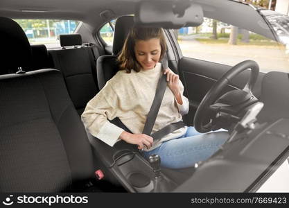 safety, car driving and people concept - happy smiling young woman or female driver fastening seat belt. woman or female driver fastening seat belt in car