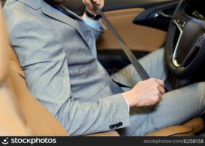 safety, driving and people concept - close up of man in elegant business suit fastening seat safety belt in car