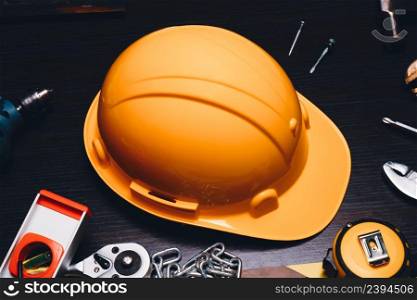 Safety helmet, hard hat with yellow color on the wooden table and mechanic tools alongside