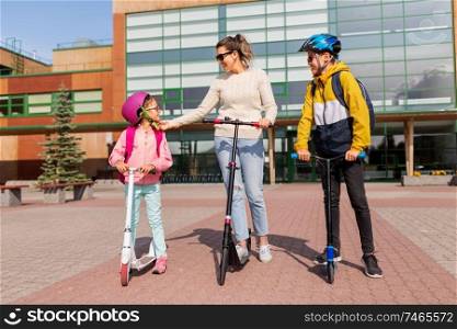 safety, school and family concept - happy daughter, son and mother riding scooters outdoors. happy school children with mother riding scooters