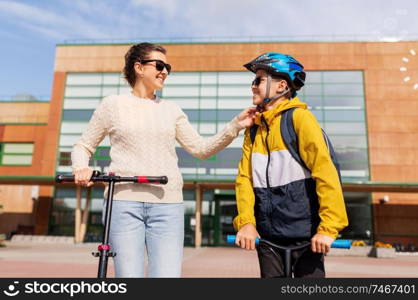 safety, school and family concept - happy mother adjusting son&rsquo;s helmet for scooter ride. mother and son in helmet with schooter near school