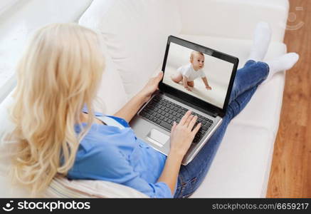 safety, technology and family concept - mother watching her baby by video monitor on laptop computer at home. mother watching baby by video monitor on laptop