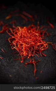 Saffron dry petals spices heap on dark slate stone table. Saffron flavor and coloring seasoning ingredient.