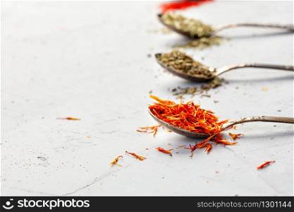 Saffron seasoning in an old silver spoon on the background of other spices in blur on a gray concrete background. Side view, copy space.. Saffron seasoning in an old silver spoon on the background of other seasonings in blur on a gray concrete background.
