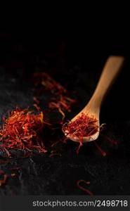 Saffron spices heap and in wooden spoon on black slate stone table. Saffron flavor and coloring seasoning ingredient.