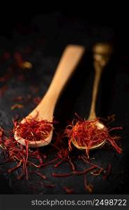 Saffron spices threads in spoons on black slate stone table. Saffron flavor and coloring seasoning ingredient.