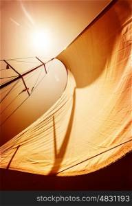 Sail fluttering in the wind on orange sky background, mild sunset light, sea cruise on luxury sailboat, summer vacation and holidays concept