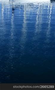 Sailboat blurred mast reflexion on the marina blue sea water