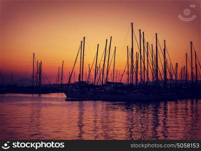 Sailboat harbor on sunset, silhouettes of luxury water transport in red and yellow evening sun light, beautiful view on port in Greece