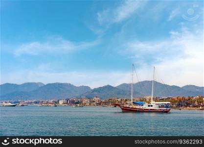 Sailboat in the sea over mountains and seaside resort town background. Summer vacation, adventure, travel, active leisure.
