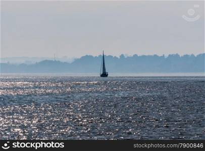 Sailboat on water against hazy shoreline silhouette.