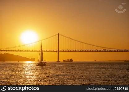 Sailboat with the Ponte 25 de Abril or 25the April Bridge at the Rio Tejo near the City of Lisbon in Portugal. Portugal, Lisbon, October, 2021