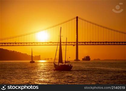 Sailboat with the Ponte 25 de Abril or 25the April Bridge at the Rio Tejo near the City of Lisbon in Portugal. Portugal, Lisbon, October, 2021