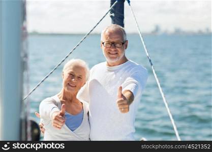 sailing, age, tourism, travel and people concept - happy senior couple hugging on sail boat or yacht deck floating and showing thumbs up in sea