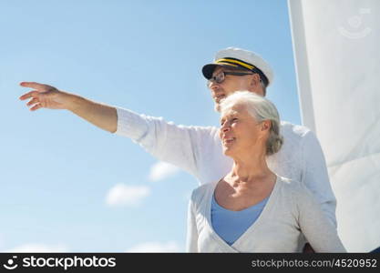 sailing, age, tourism, travel and people concept - happy senior couple pointing finger on sail boat or yacht deck floating in sea