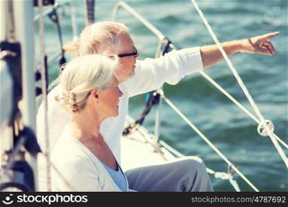 sailing, age, tourism, travel and people concept - happy senior couple pointing finger on sail boat or yacht deck floating in sea