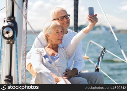 sailing, age, tourism, travel and people concept - happy senior couple taking selfie with smartphone on sail boat or yacht deck floating in sea