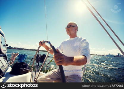 sailing, age, tourism, travel and people concept - happy senior man in captain hat on steering wheel and navigating sail boat or yacht floating in sea