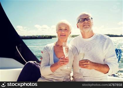 sailing, age, travel, holidays and people concept - happy senior couple with champagne glasses on sail boat or yacht deck floating in sea