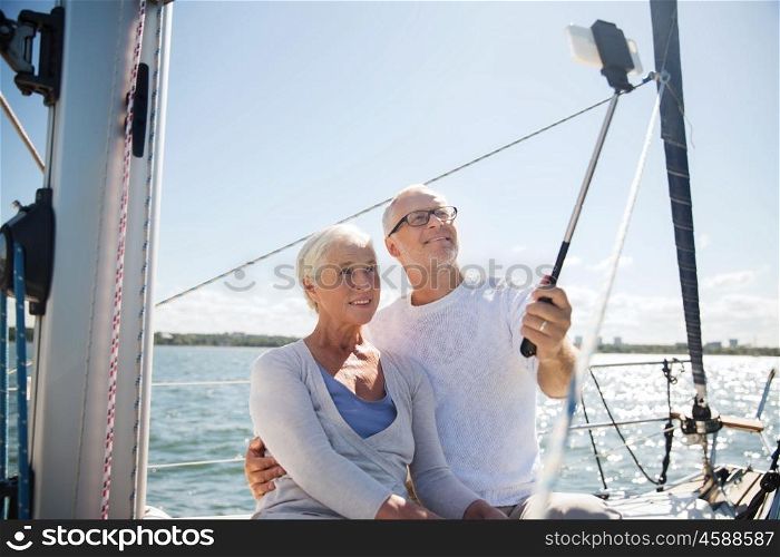 sailing, age, travel, technology and people concept - happy senior couple with smartphone selfie stick taking picture on sail boat or yacht deck floating in sea