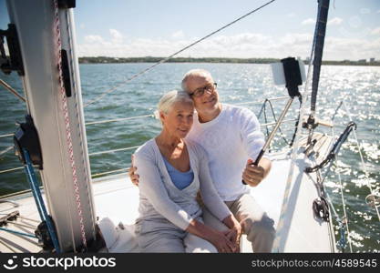 sailing, age, travel, technology and people concept - happy senior couple with smartphone selfie stick taking picture on sail boat or yacht deck floating in sea