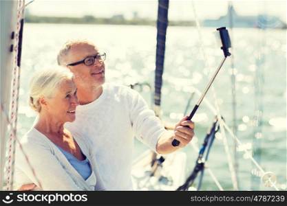 sailing, age, travel, technology and people concept - happy senior couple with smartphone selfie stick taking picture on sail boat or yacht deck floating in sea