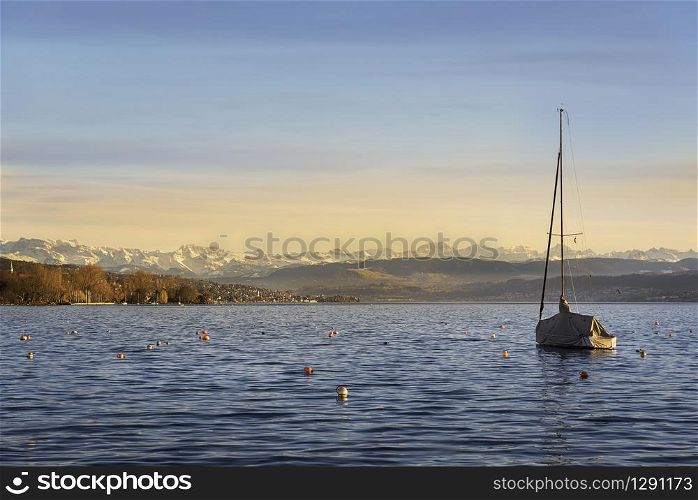 Sailing boat anchored on Zurich lake at sunset. Landscape with Zurich lake and swiss mountain skyline.