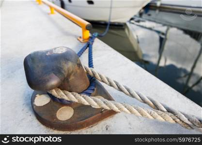 sailing, safety, mooring and water transport concept - rusted iron mooring bollard with rope on concrete pier