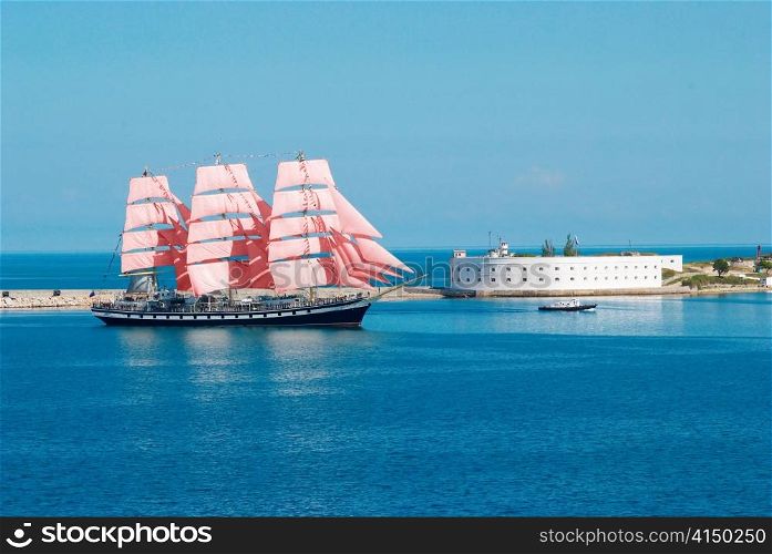 Sailing ship with red sails entering to the bay.