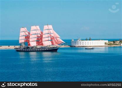 Sailing ship with red sails entering to the bay.