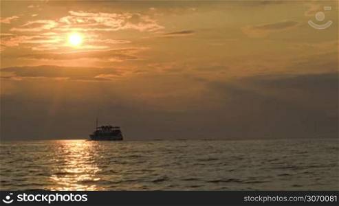 Sailing small ship in quiet open sea at sunset. Water sparkling in dim sunlight