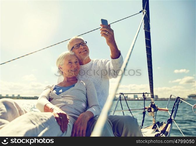 sailing, technology, tourism, travel and people concept - happy senior couple taking selfie with smartphone on sail boat or yacht deck floating in sea