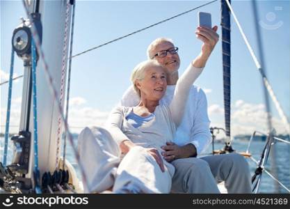 sailing, technology, tourism, travel and people concept - happy senior couple with smartphone taking selfie on sail boat or yacht deck floating in sea