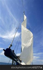 Sailor in sailboat rigging the sails over sunny summer blue sky