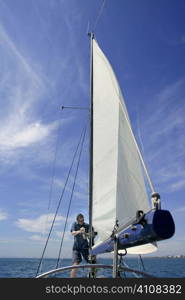 Sailor in sailboat rigging the sails over sunny summer blue sky