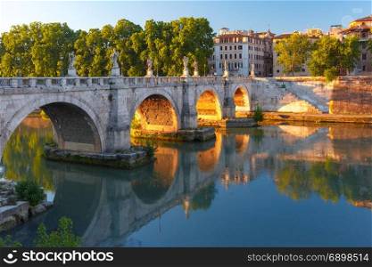 Saint Angel bridge at sunrise, Rome, Italy.. Saint Angel bridge with mirror reflection in Tiber River at sunset in Rome, Italy.