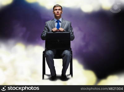 Saint businessman. Young businessman with halo above head sitting on chair