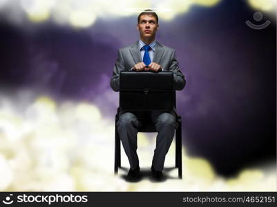 Saint businessman. Young businessman with halo above head sitting on chair